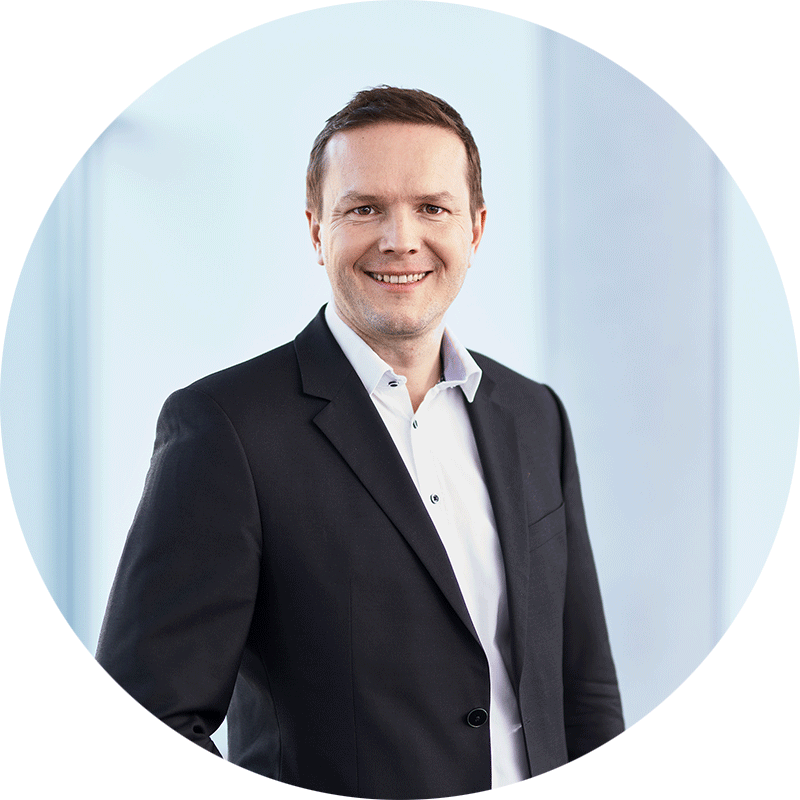 joerg-seidel-rund Smiling businessman in a black suit and white shirt, circular headshot.